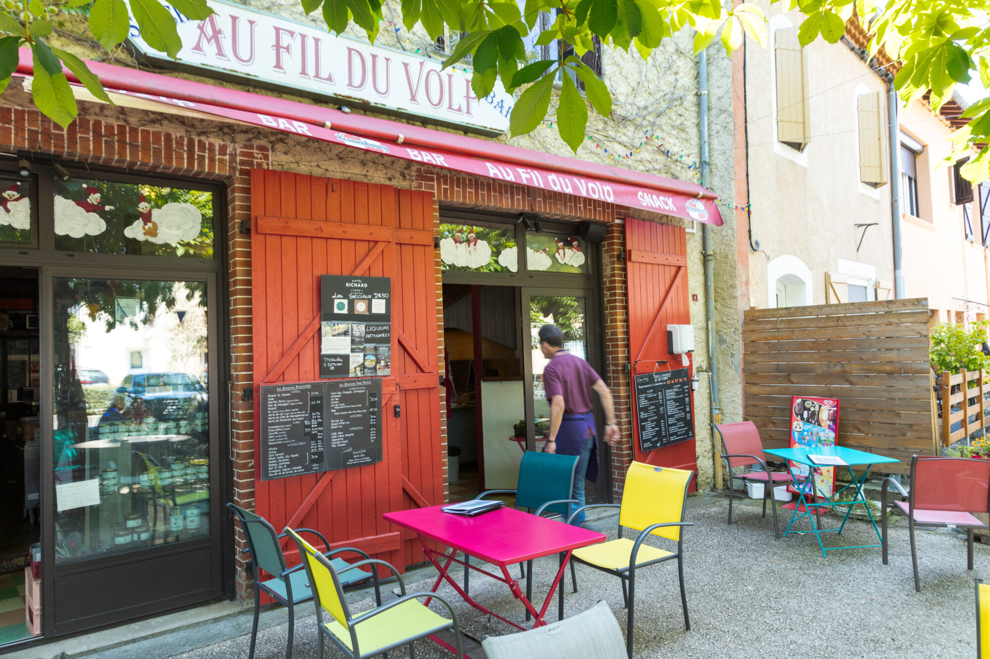 Terrasse du bar Au Fil du Volp avec tables colorées en extérieur