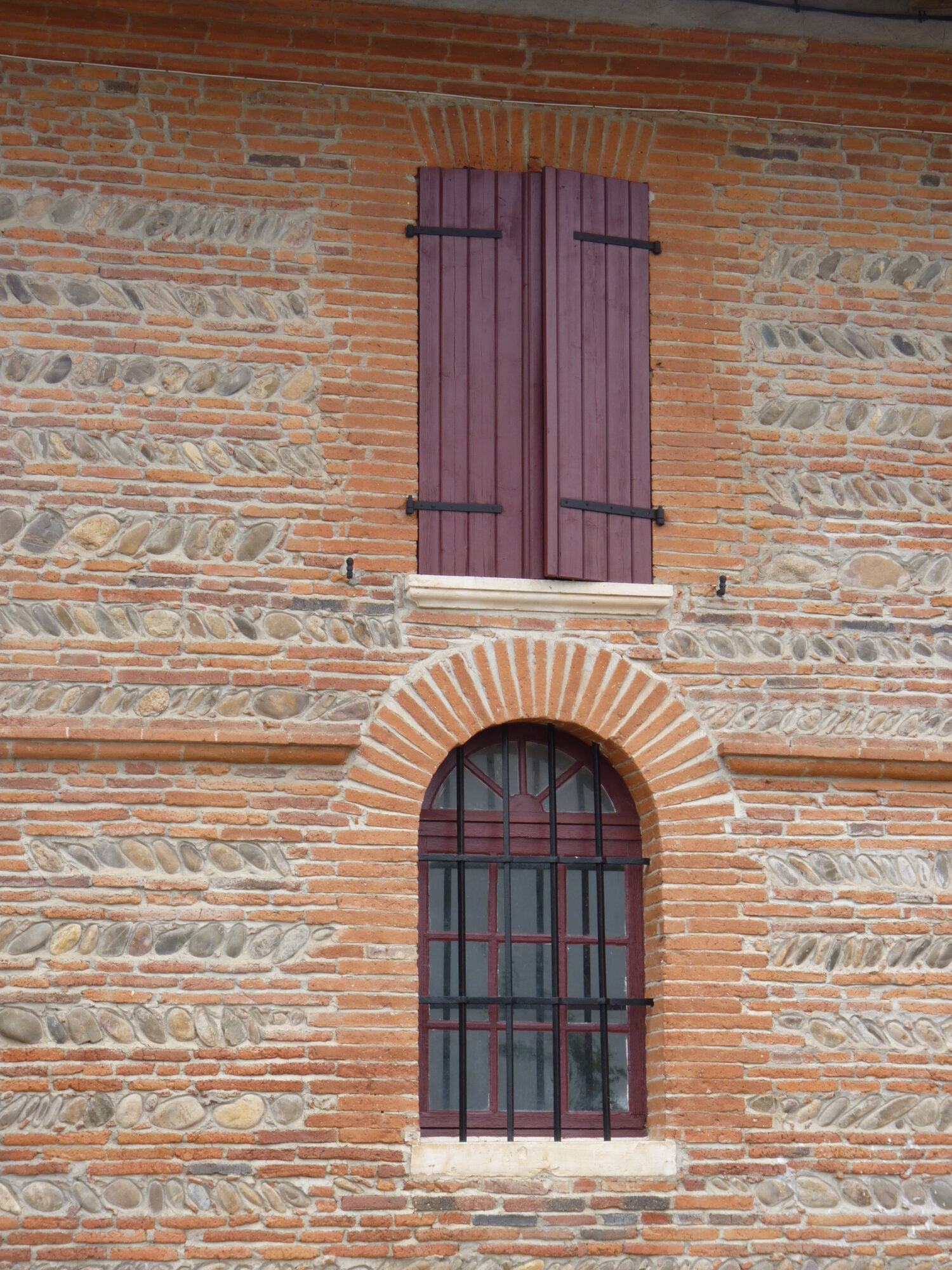 Façade en briques et galets avec volets clos et fenêtre cintrée