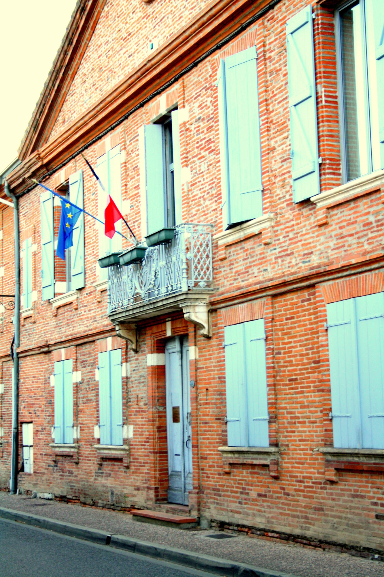 Façade en brique avec volets bleus et drapeaux, Office de Tourisme Cœur de
