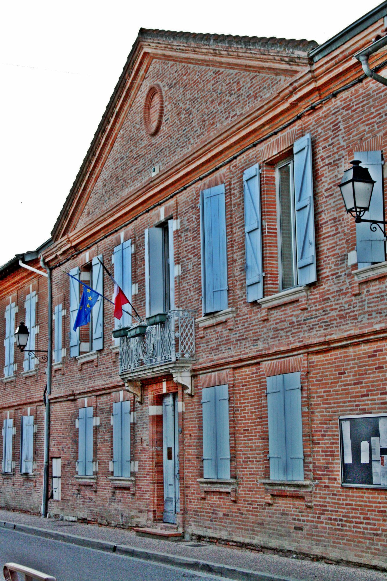 Façade de mairie en brique avec volets bleus et drapeaux français et européen