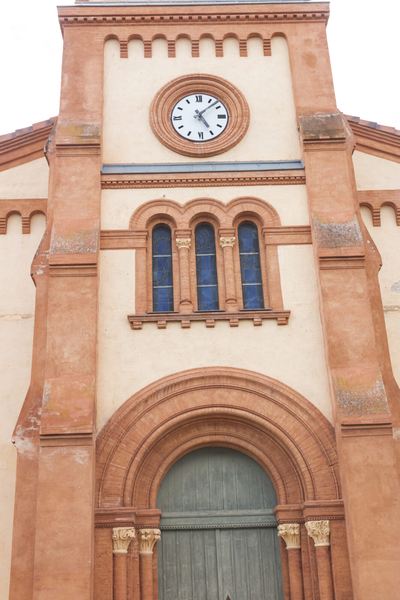 Façade d’église en briques roses avec horloge et portail cintré