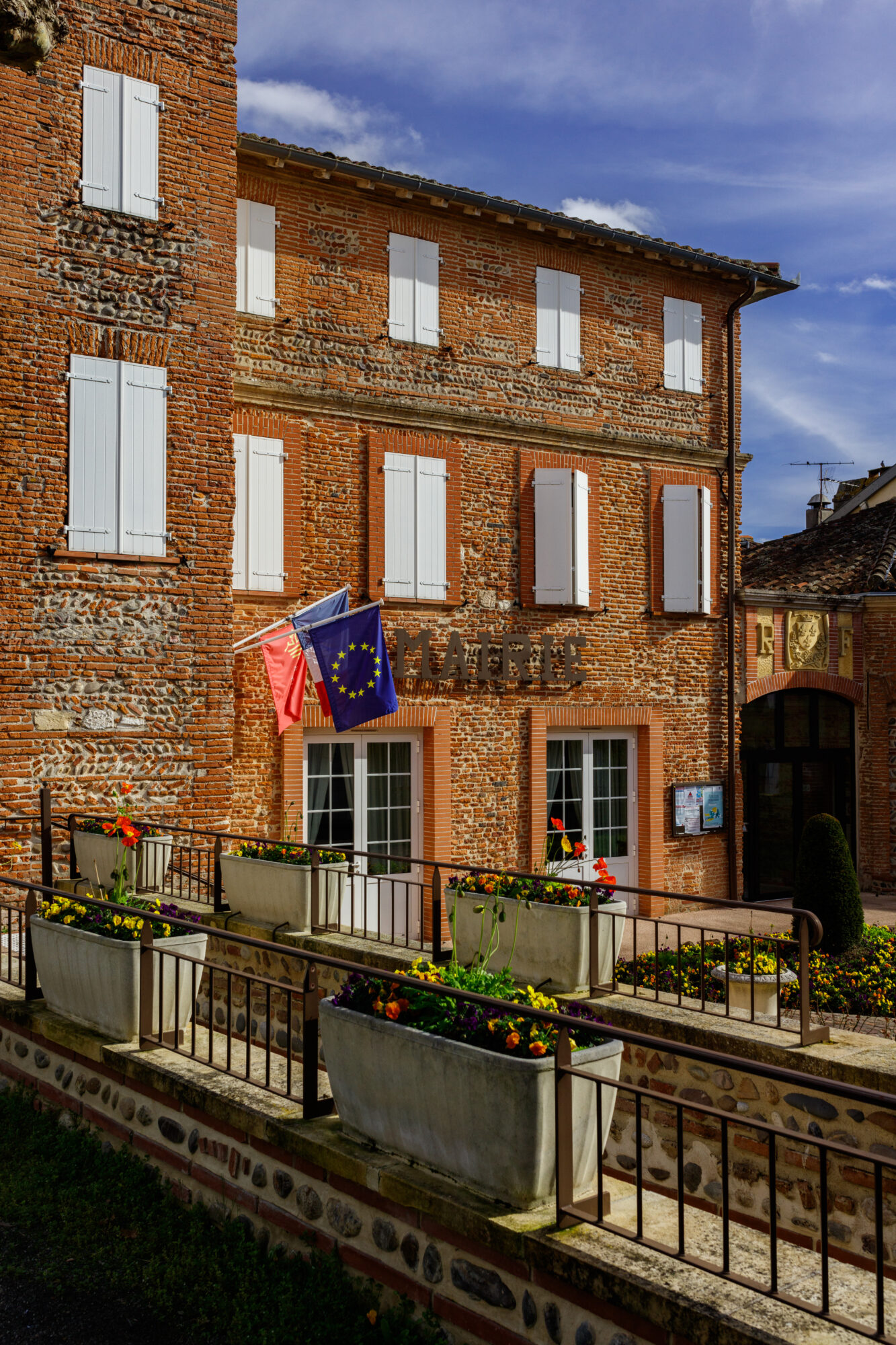 Façade de mairie en briques avec volets blancs et drapeaux français et européen