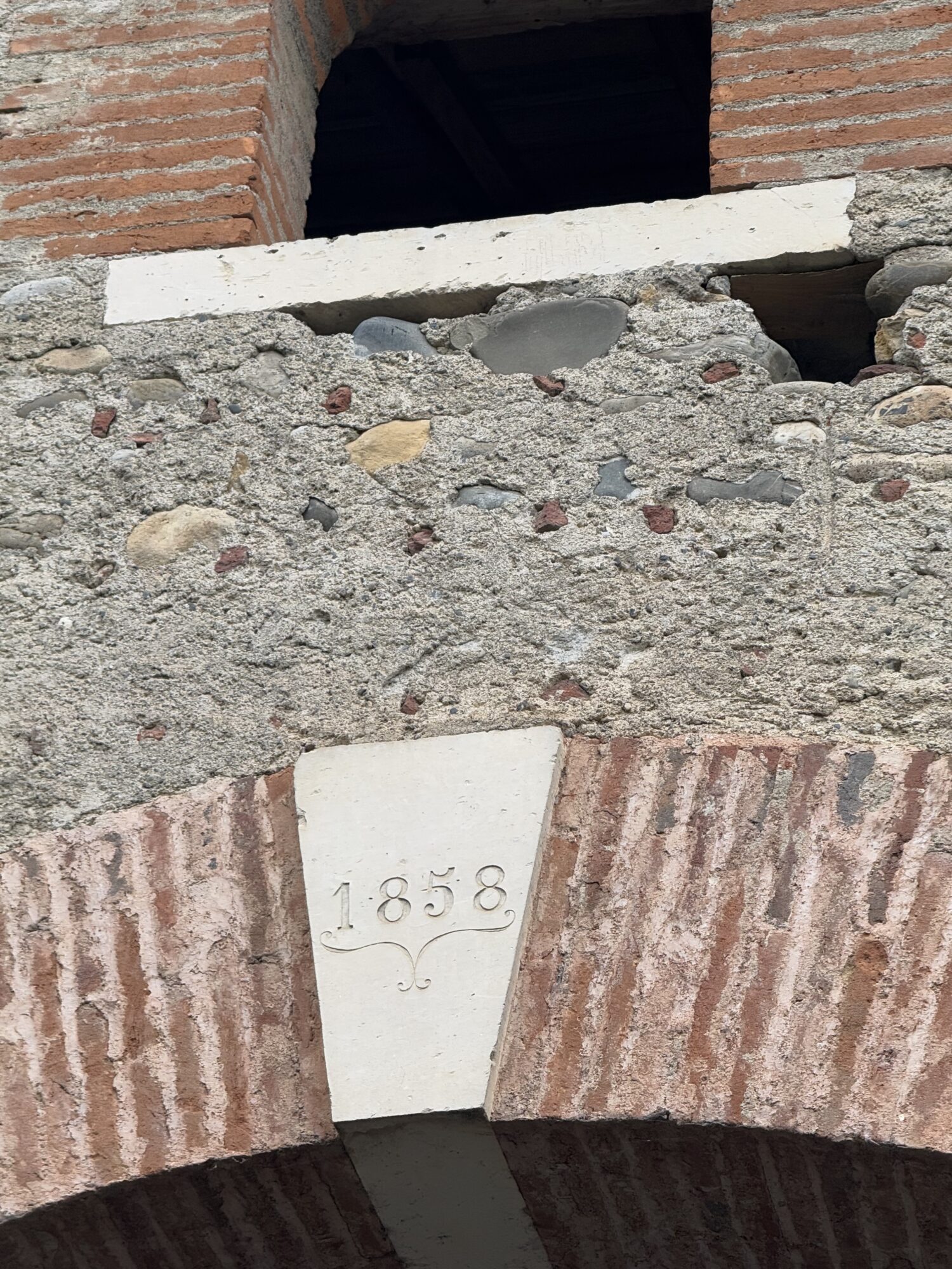 Clé de voûte datée 1858 sur arche en brique et galets