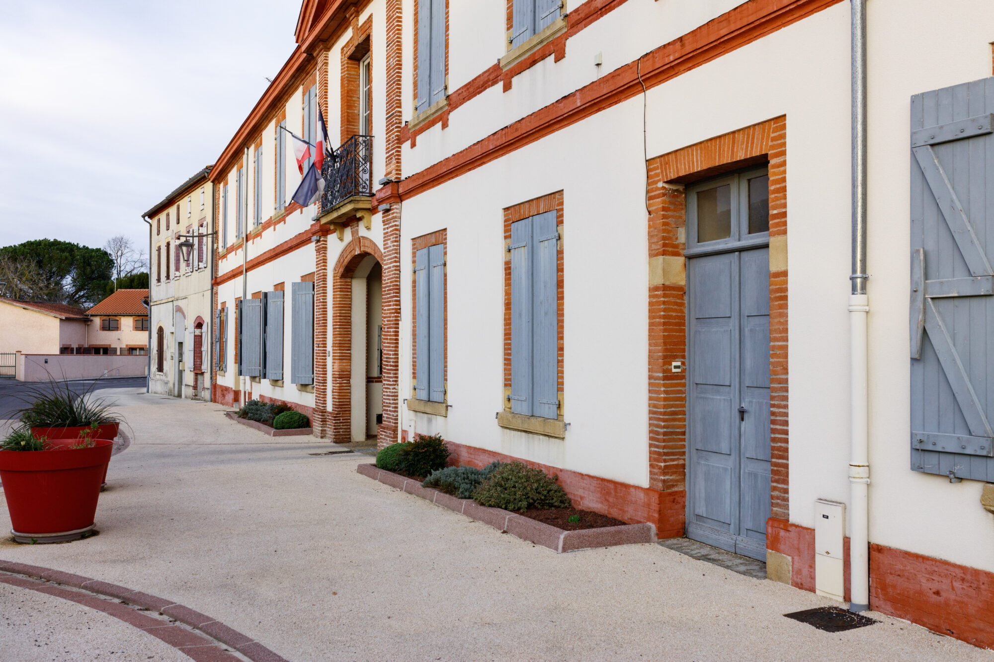 Façade de mairie en brique et volets bleus avec drapeaux français