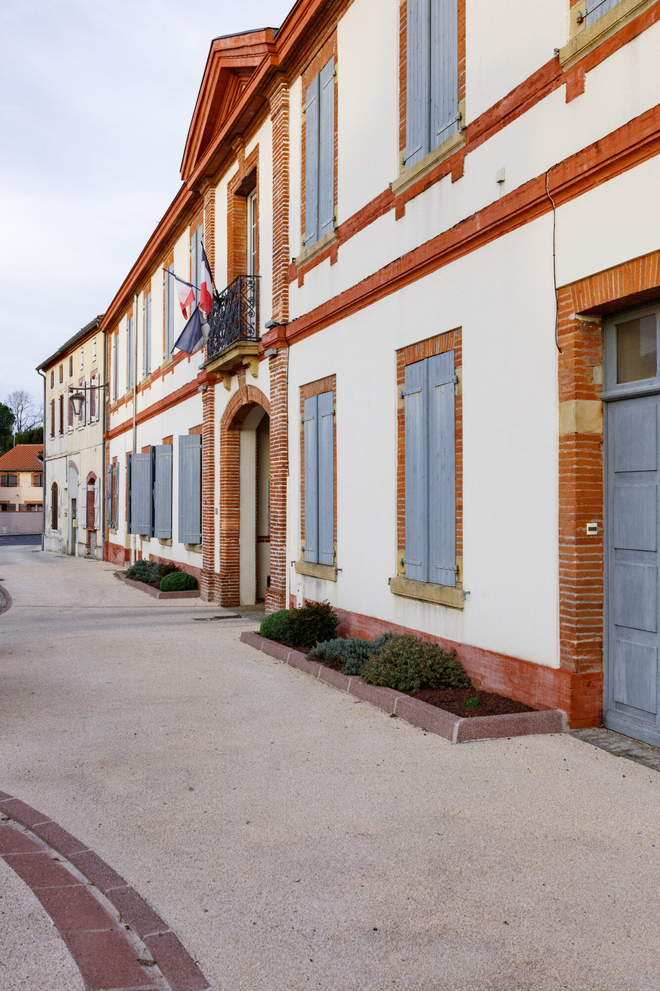 Façade de mairie en briques et volets bleus avec drapeaux français