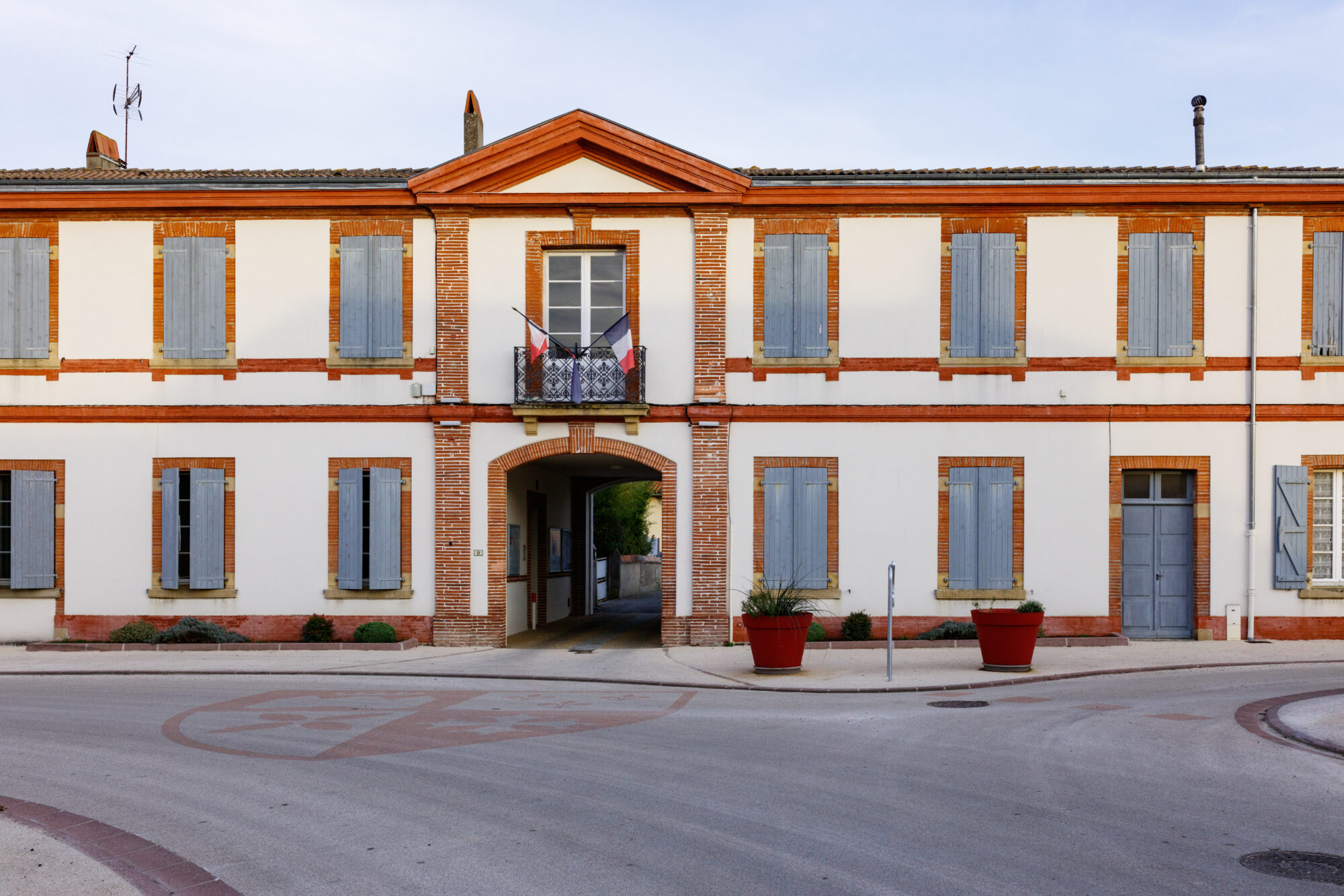 Façade de mairie en brique et volets bleus avec drapeaux français