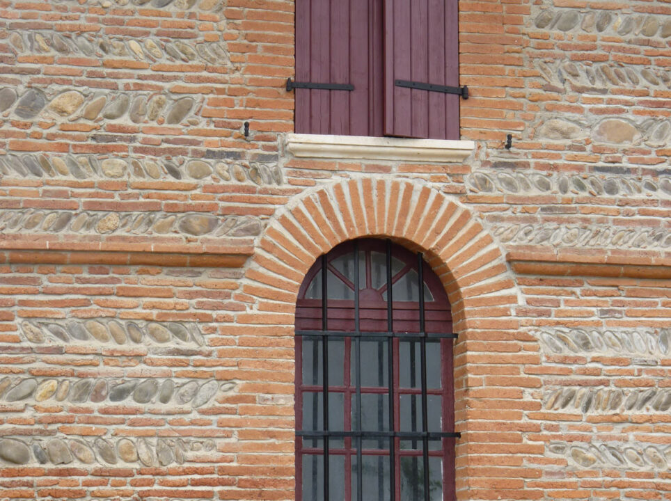 Façade en briques et galets avec fenêtre cintrée et volets en bois