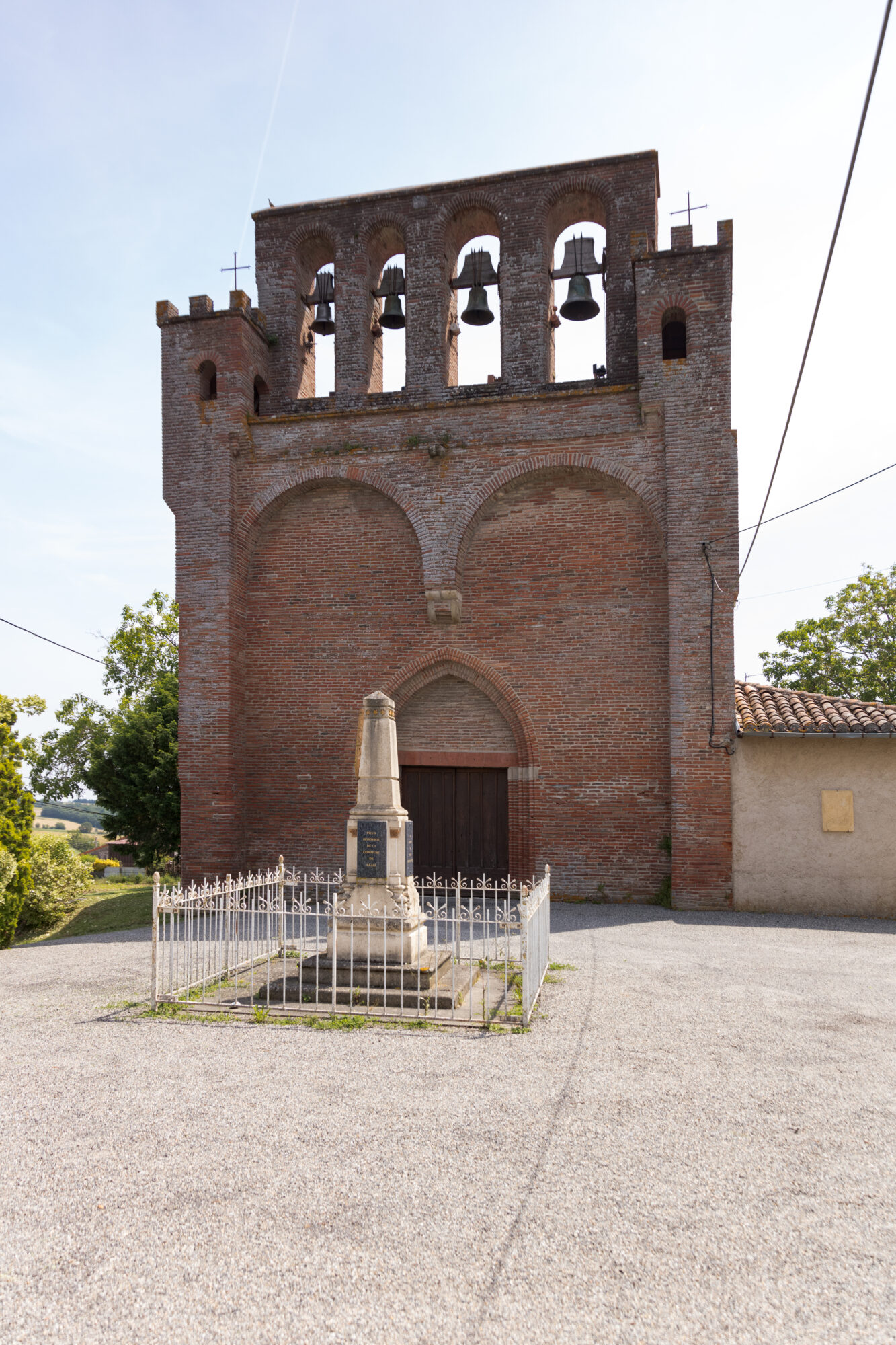 Façade en brique d'une église à clocher-mur et monument aux morts