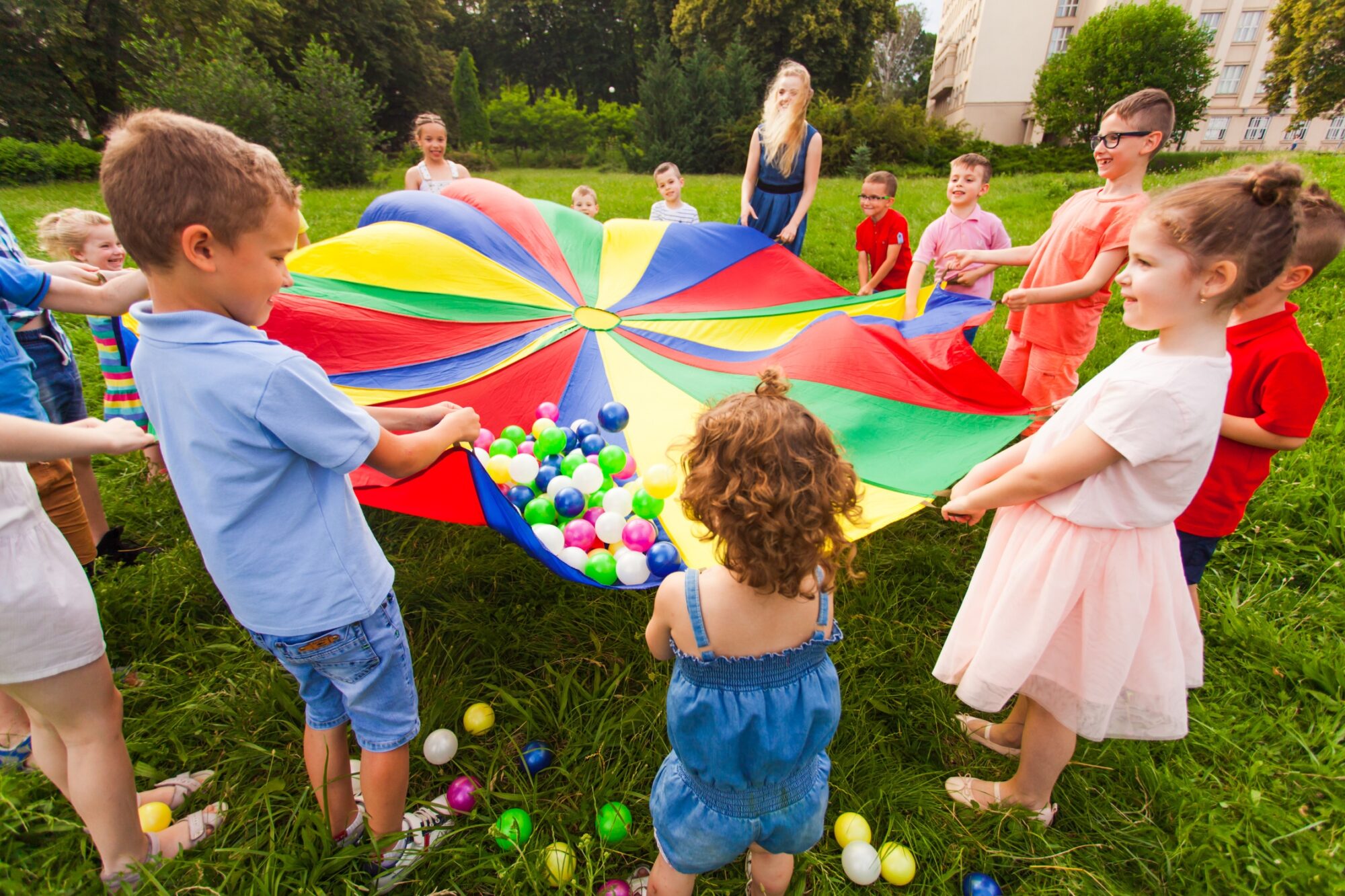 Enfants jouant avec un parachute multicolore et des balles colorées
