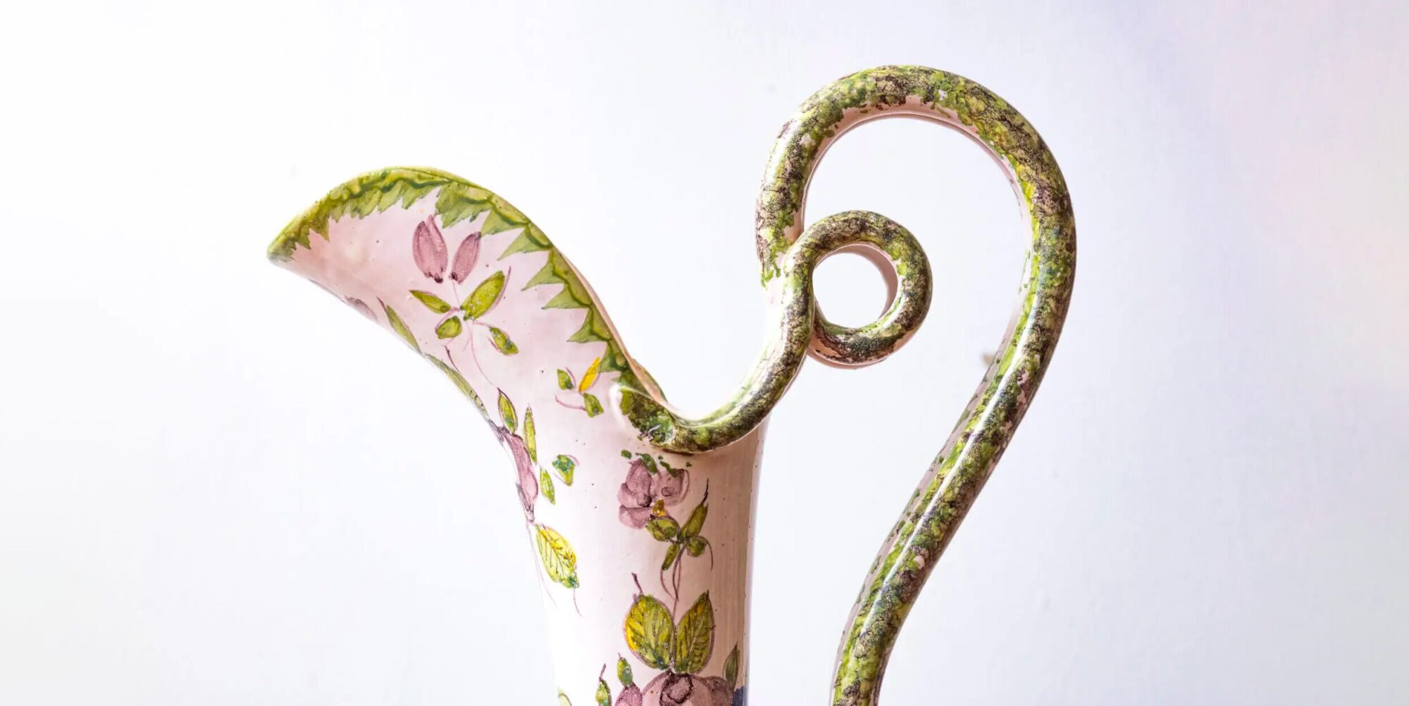 Détail d'un pichet en céramique peint à motifs floraux et anse spiralée