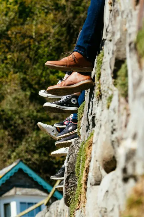 Jambes et chaussures de visiteurs assis sur un mur en pierre