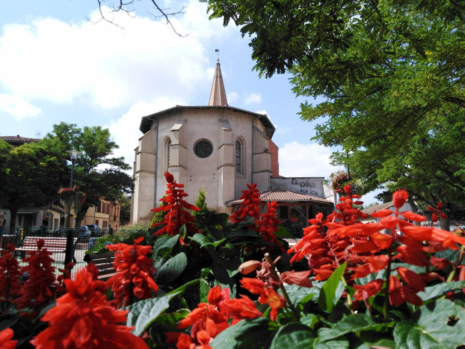 Église au clocher pointu vue depuis un parterre de fleurs rouges