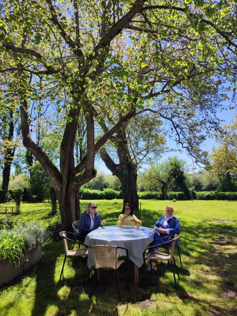 Trois personnes attablées en terrasse dans un jardin ombragé