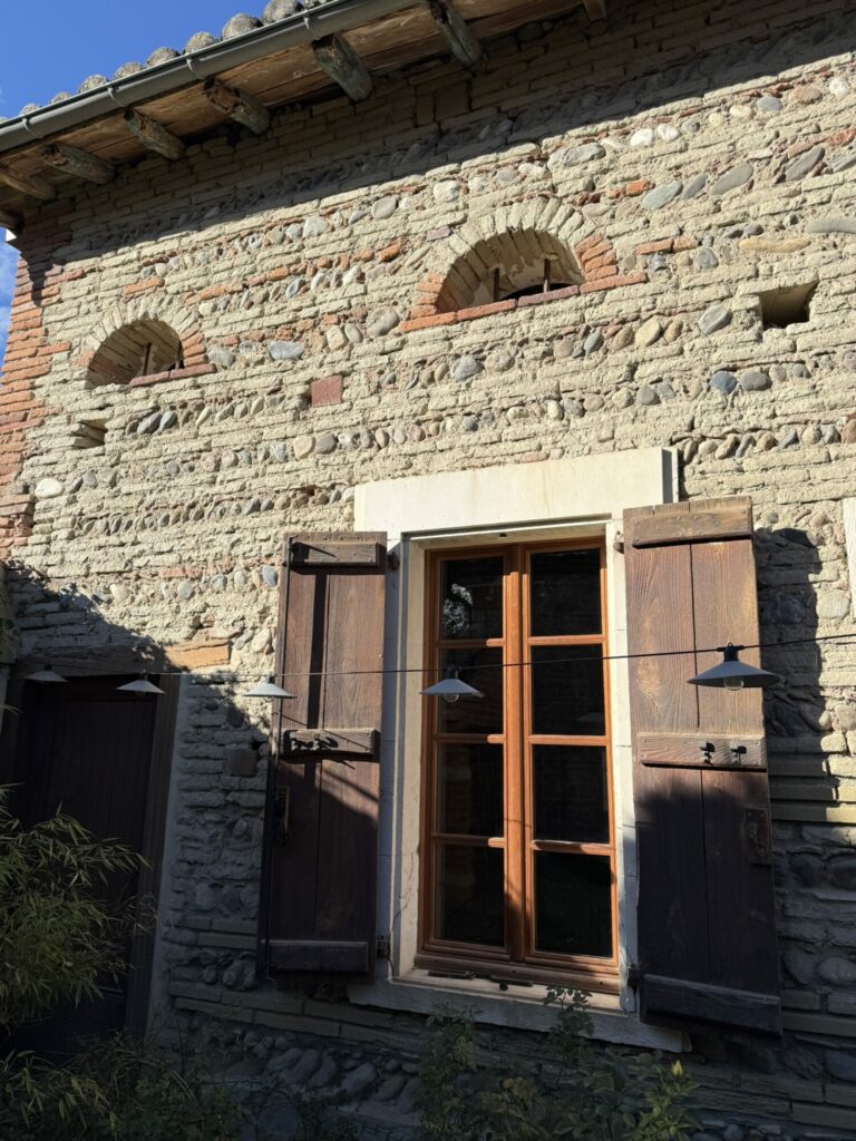 Façade en galets et brique avec fenêtre à volets en bois