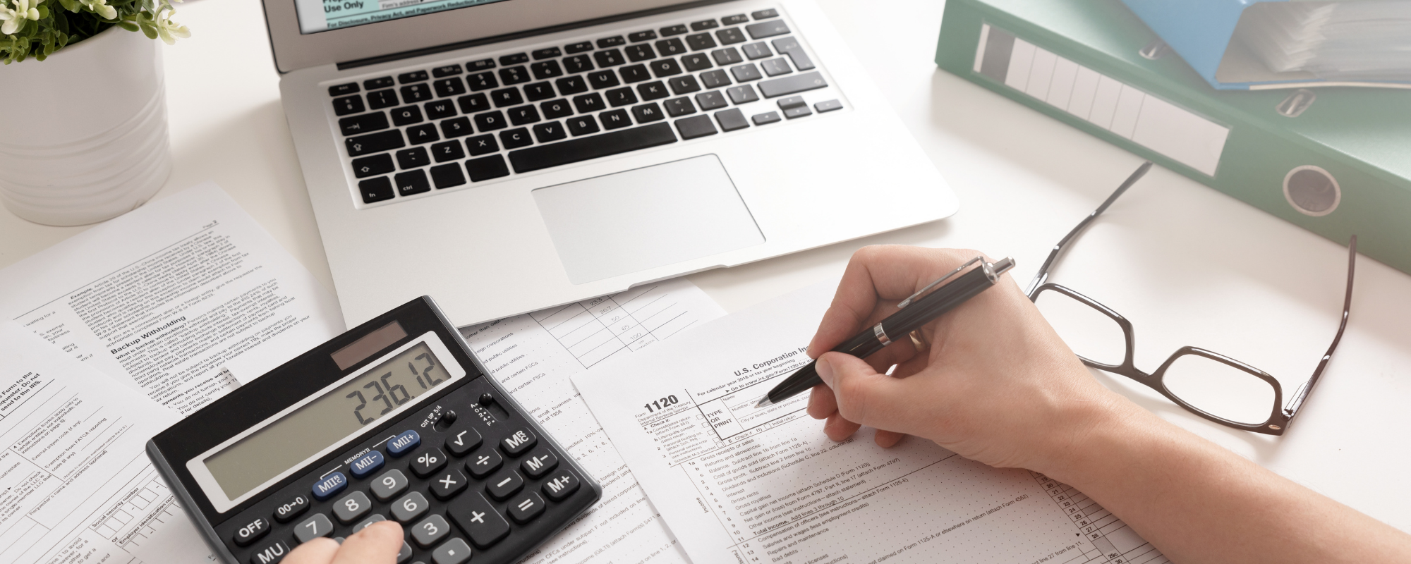 Main remplissant un formulaire avec calculatrice, ordinateur et lunettes