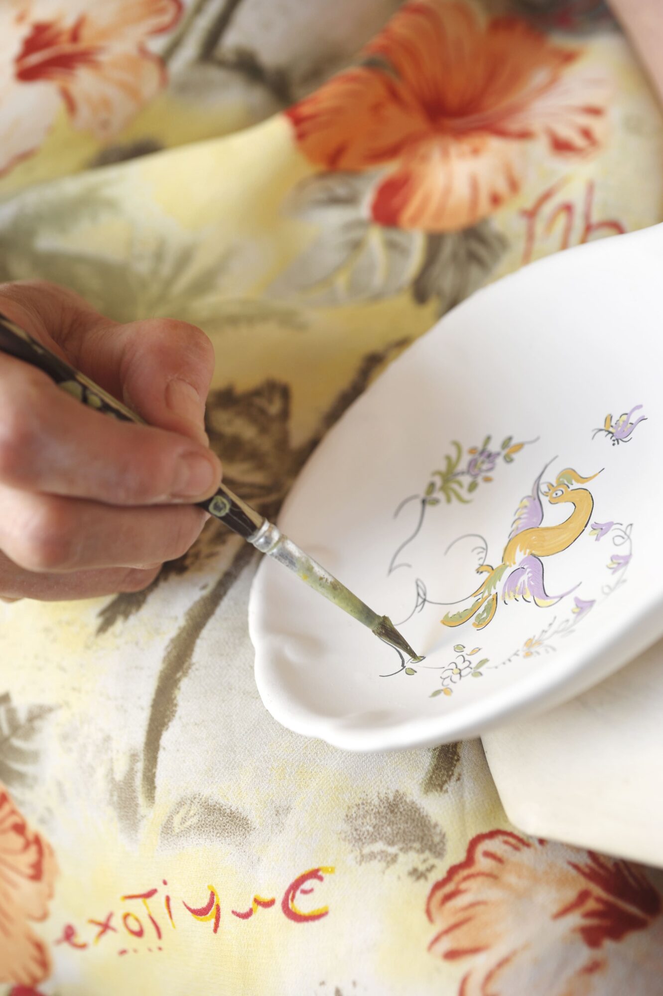 Main peignant un motif floral sur une assiette en céramique artisanale