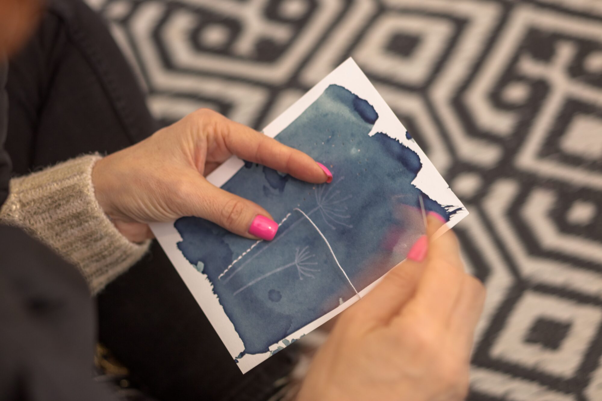 Personne réalisant une carte en aquarelle bleue avec motif floral blanc