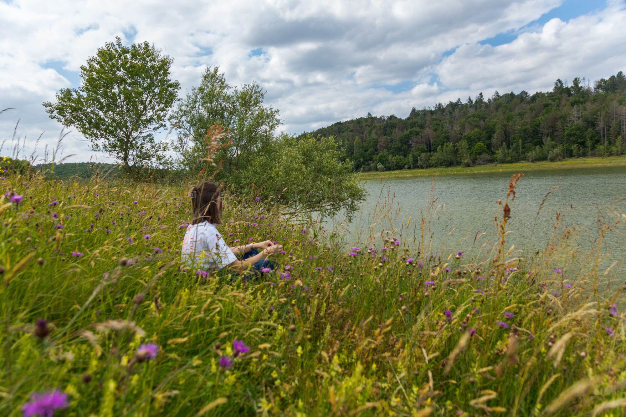 Personne assise dans l’herbe au bord d’un lac, Office de Tourisme Cœur de