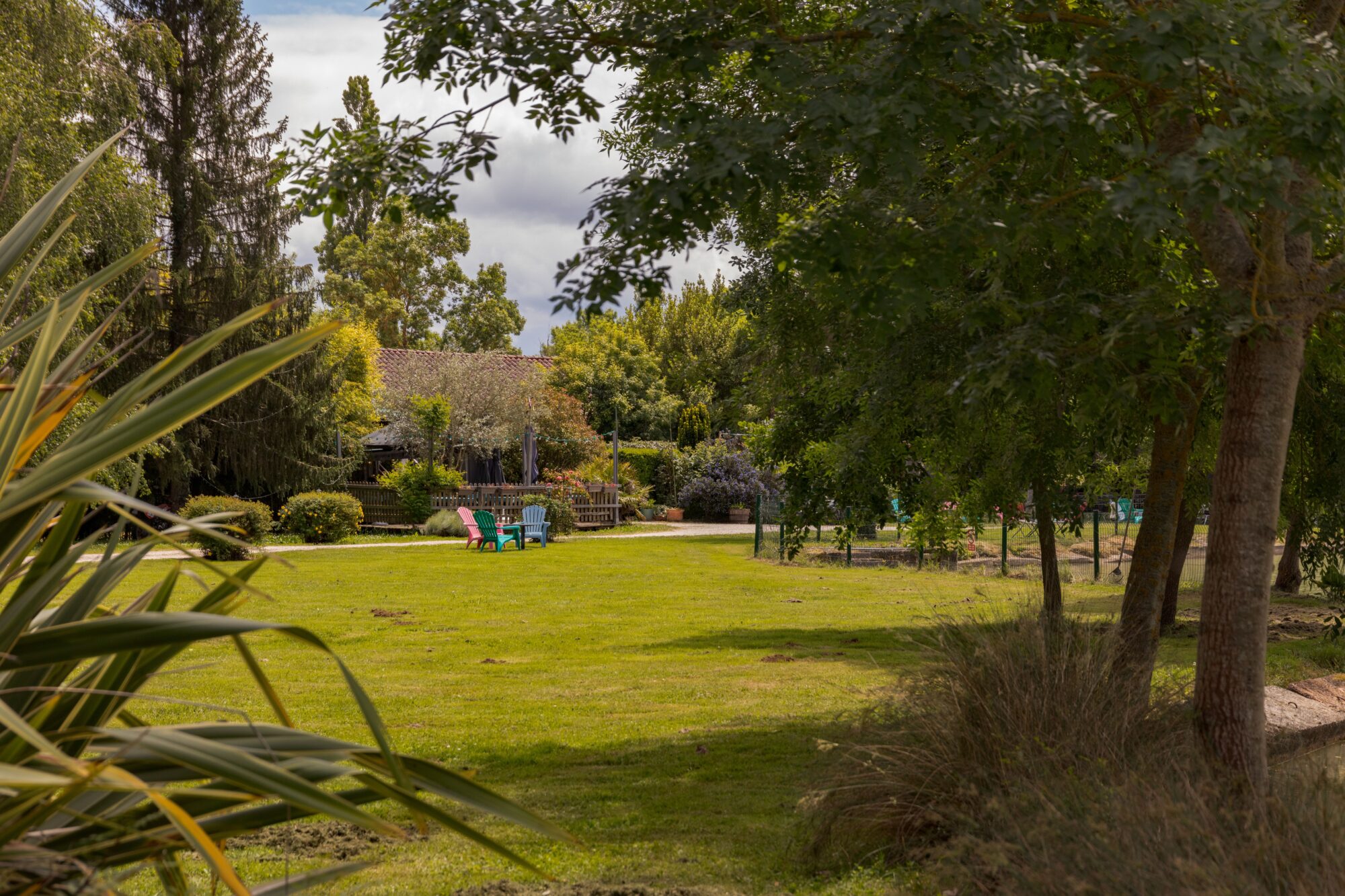 Jardin arboré avec pelouse et chaises colorées, Office de Tourisme Cœur de