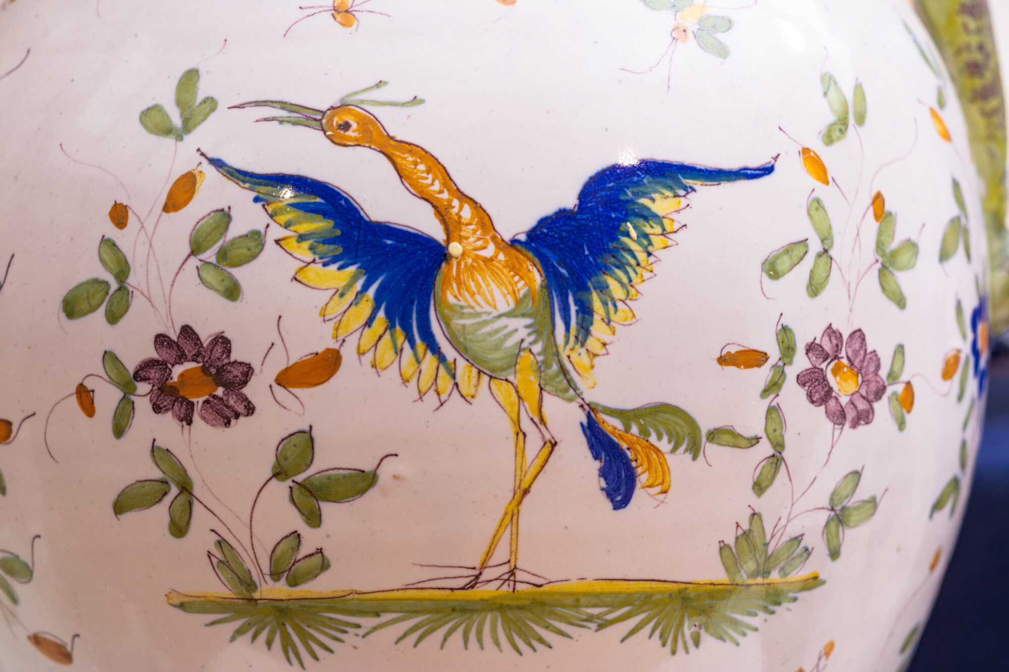 Oiseau peint bleu et jaune sur céramique décorée de motifs floraux