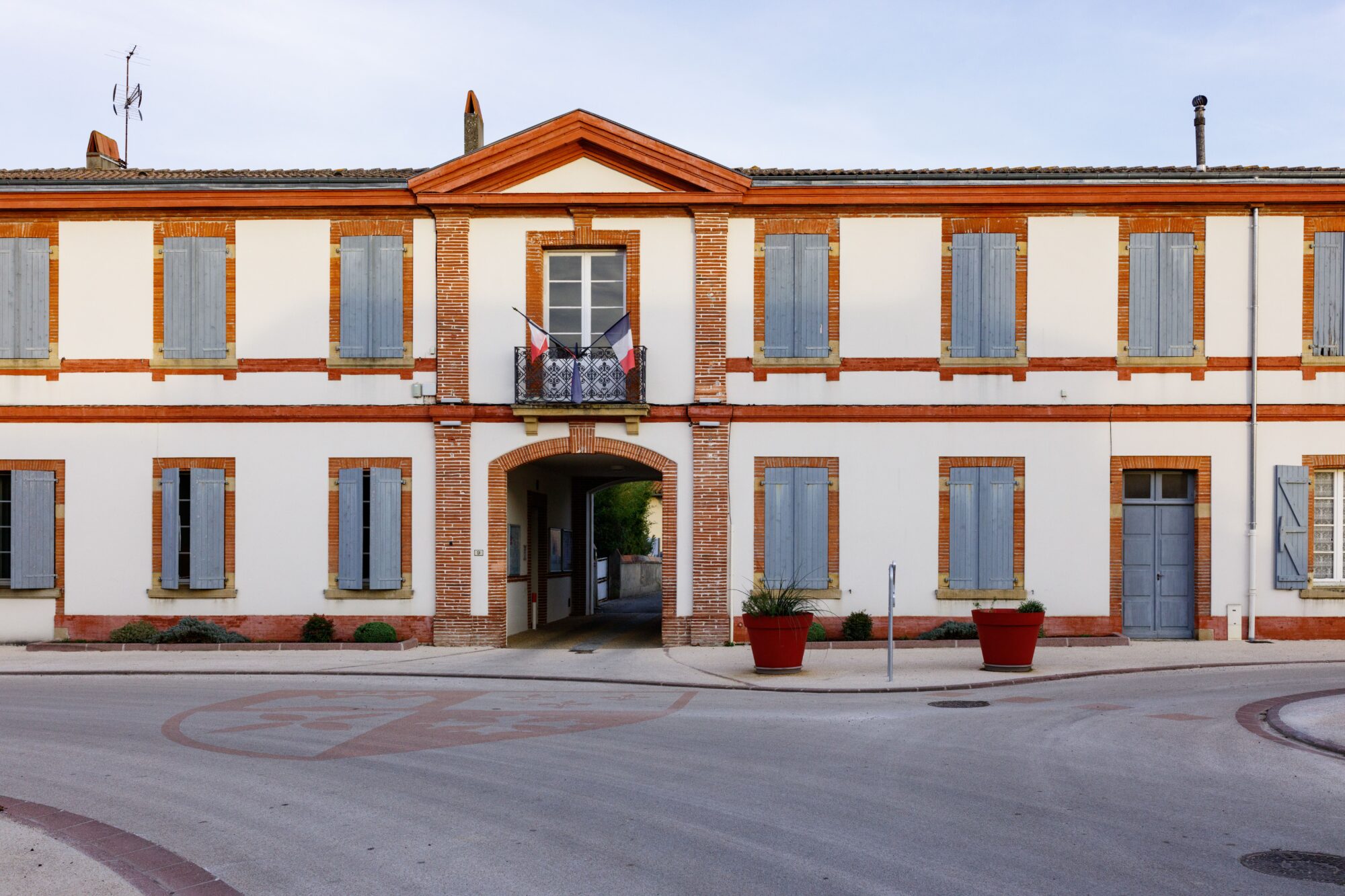 Façade de mairie en brique et volets bleus avec drapeaux français