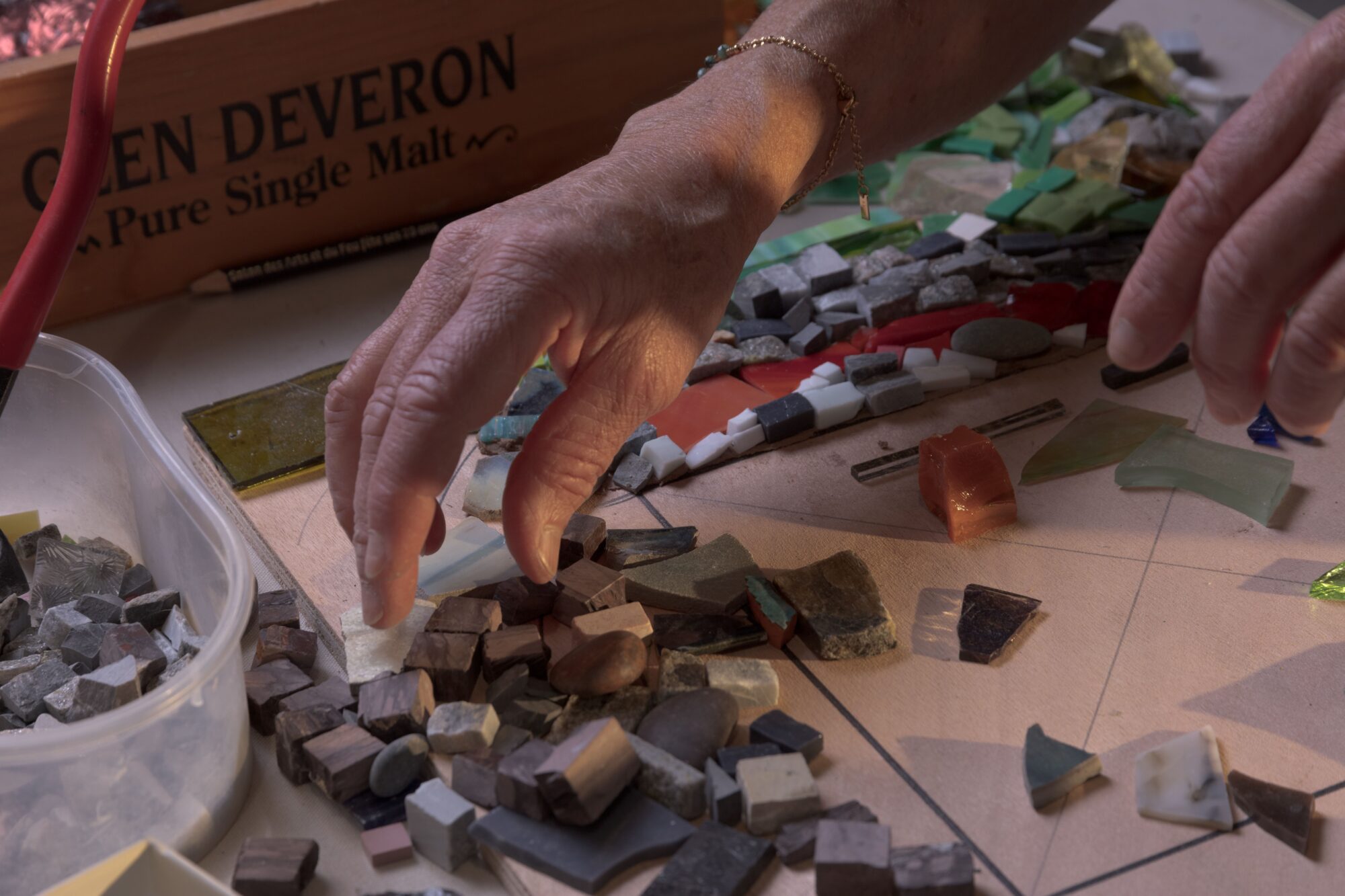 Mains assemblant une mosaïque artisanale en tesselles de pierre et verre