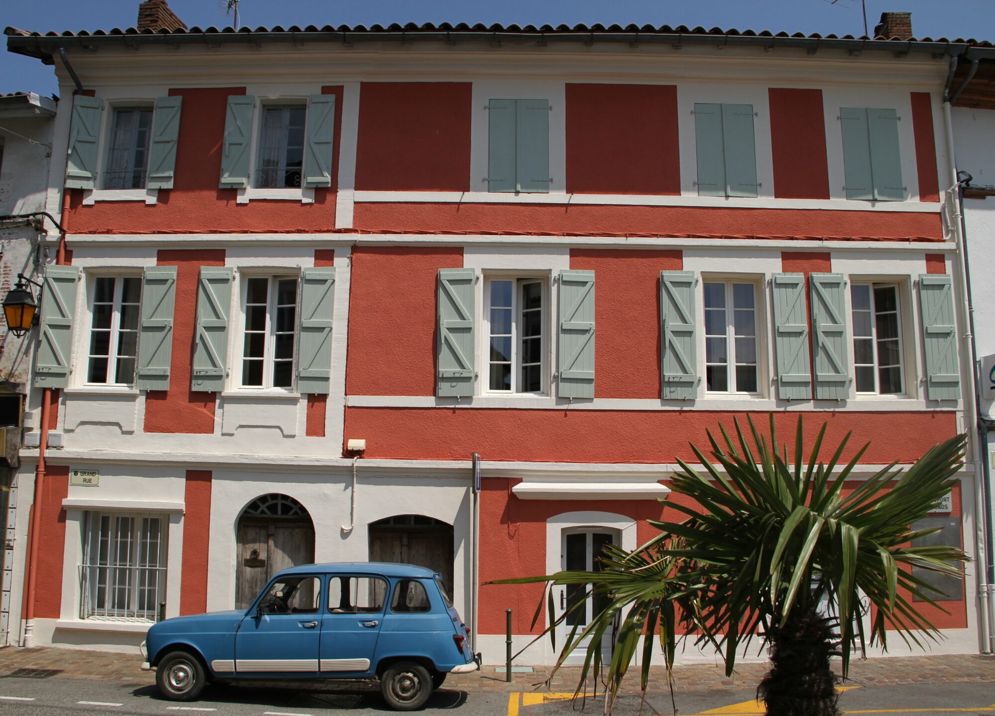 Façade rouge et blanche à volets bleus, Office de Tourisme Cœur de Garonne